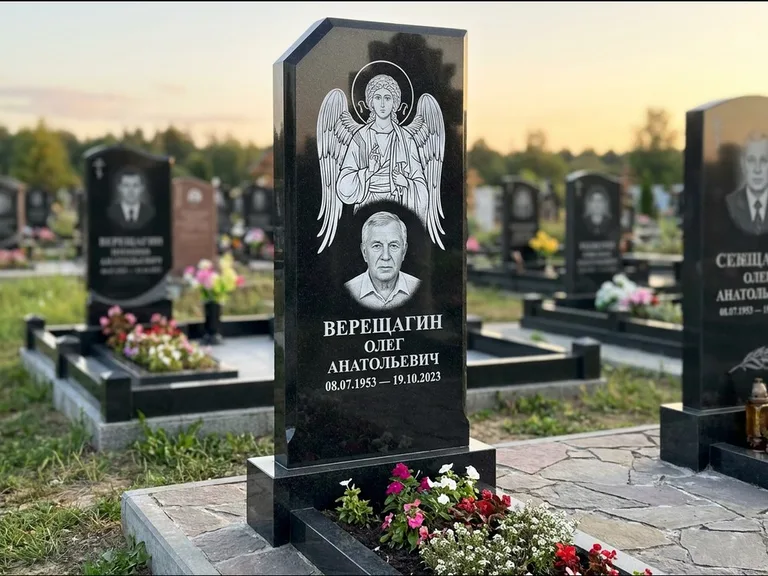 Памятник с гравировкой иконы: стела с резным навершием и нимбом в золоте — гравировка образа Спасителя, высокие разросшиеся туи полукругом, работа «Мельникова» в Красноярске