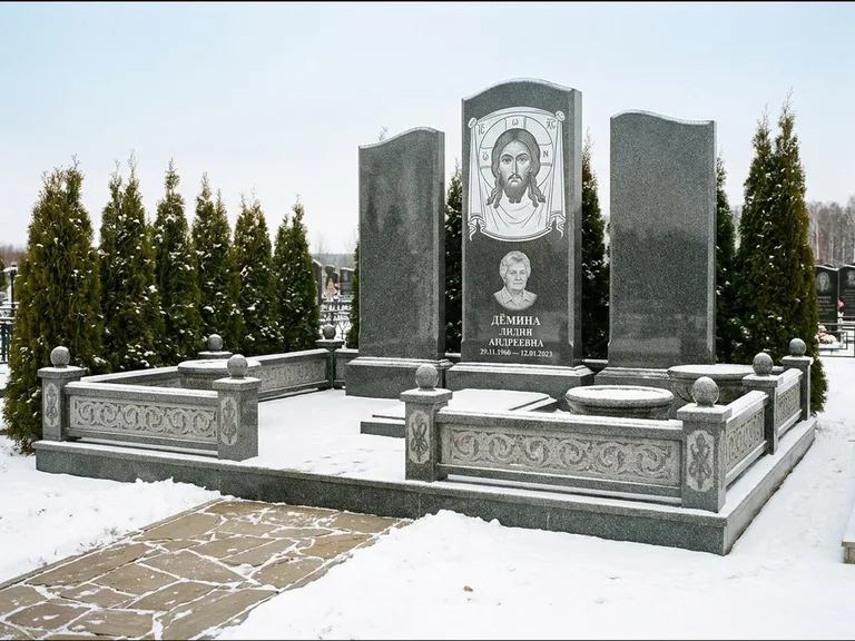 Памятник с гравировкой иконы: узкая вертикальная стела-пилон с ликом — икона в резной рамке-киоте, открытая лужайка без ограды, работа «Одинцов» в Красноярске