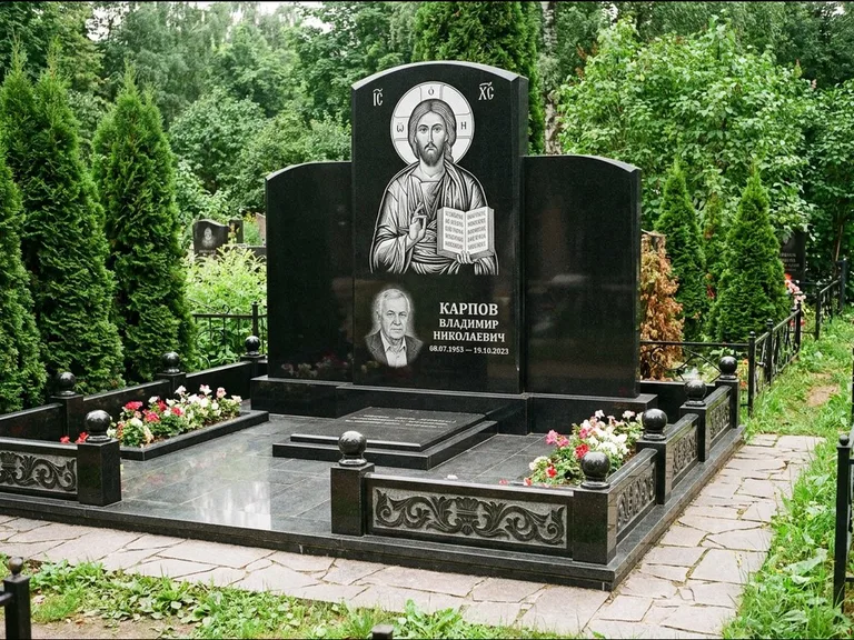 Памятник с гравировкой иконы: широкая панорамная стела с золочёным нимбом — гравировка образа Матроны Московской, цветник с белыми хризантемами, работа «Мельникова» в Красноярске