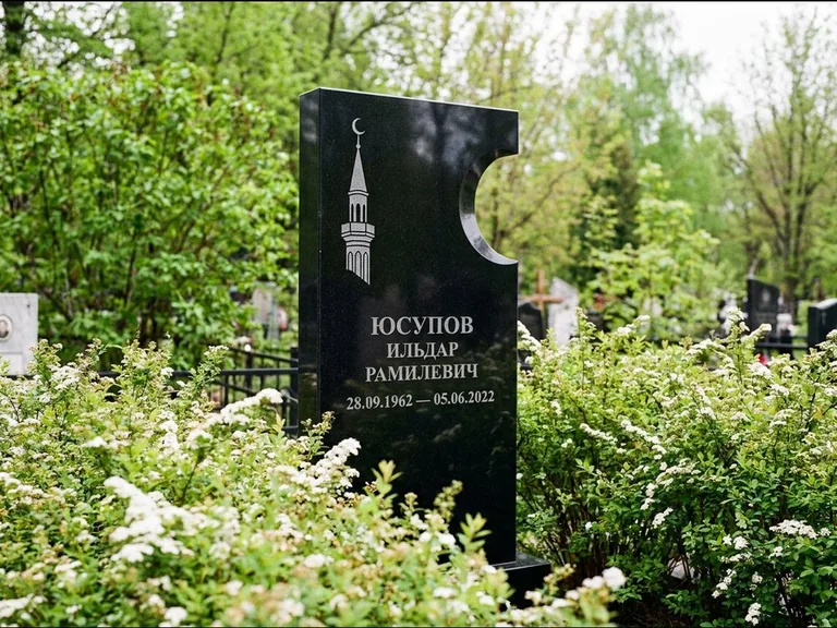 Мусульманский памятник с гравировкой мечети: стела с боковым вырезом в форме полумесяца — гравировка минарета с полумесяцем, низкие кусты спиреи в цвету, работа «Юсупов» в Красноярске